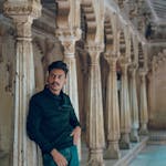 A South Asian man poses against ornate stone columns in an Indian palace.