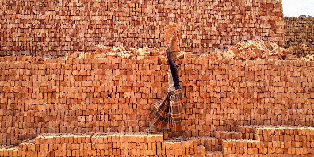 A worker balancing bricks on his head at a brick kiln in Bangladesh, showcasing hard labor.