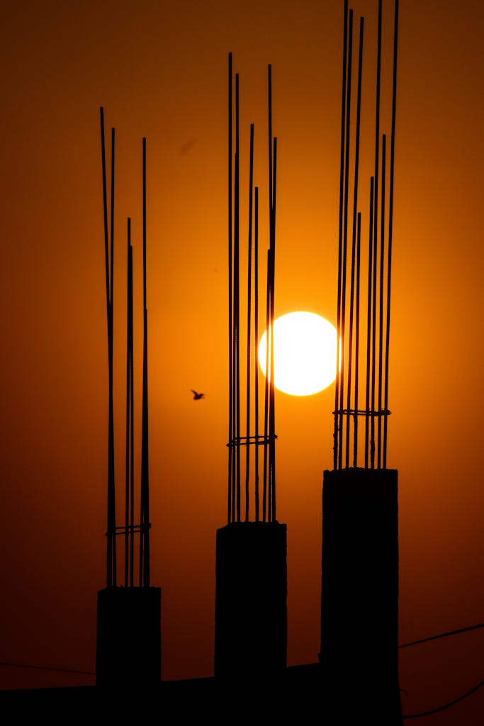 Silhouette of construction bars against a dramatic orange sunset sky, creating a striking visual.